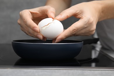 Photo of Woman breaking egg into frying pan, closeup
