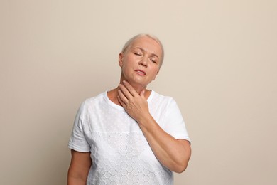 Mature woman doing thyroid self examination on beige background