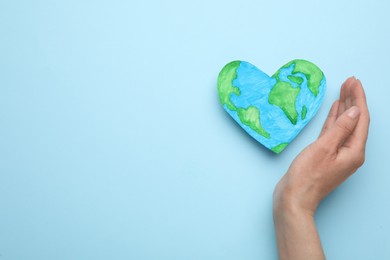 Woman and heart shaped model of planet on light blue background, top view with space for text. Earth Day