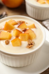 Tasty peach yogurt with granola and pieces of fruit in bowl on plate, closeup