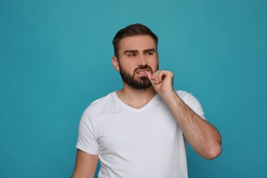 Man biting his nails on light blue background. Bad habit
