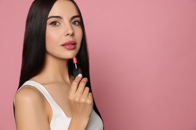 Photo of Young woman with beautiful makeup holding glossy lipstick on pink background, space for text