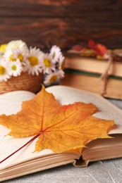 Photo of Book with autumn leaf as bookmark on light gray textured table, closeup