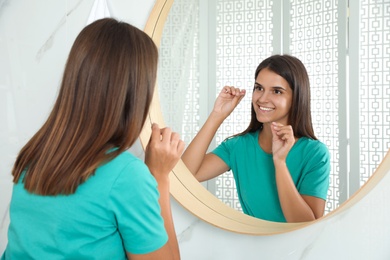 Young woman flossing her teeth in bathroom. Cosmetic dentistry