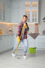 Handsome young man with headphones singing while cleaning kitchen