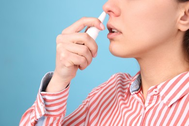 Woman using nasal spray on light blue background, closeup