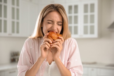 Photo of Concept of choice between healthy and junk food. Woman eating croissant in kitchen