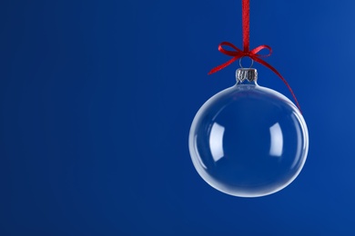 Transparent glass Christmas ball with red ribbon and bow against blue background. Space for text