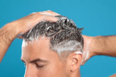 Handsome man washing hair on light blue background, closeup