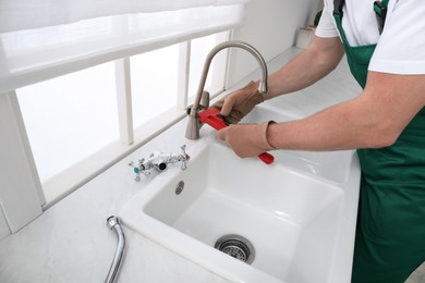 Photo of Professional plumber fixing water tap in kitchen, closeup