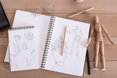Sketchbook with beautiful drawings, mannequin and pencils on wooden table, flat lay
