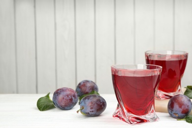 Delicious plum liquor and ripe fruits on table against white background, space for text. Homemade strong alcoholic beverage