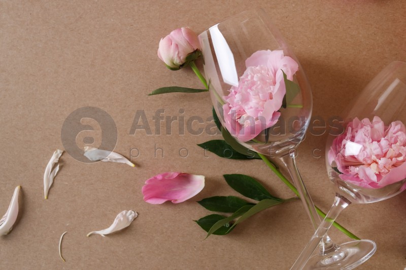 Photo of Wineglasses and beautiful pink peonies on brown background, flat lay