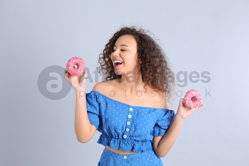 Beautiful African-American woman with donuts on light grey background