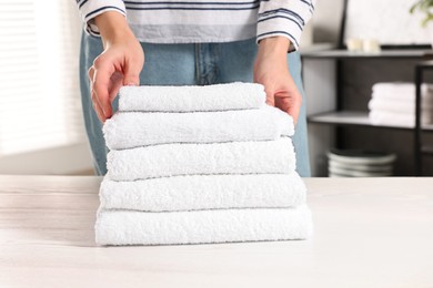 Woman stacking clean towels on white table in laundry room, closeup