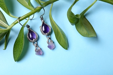 Beautiful pair of silver earrings with amethyst gemstones and leaves on light blue background, above view