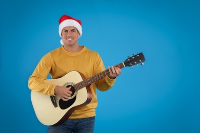 Man in Santa hat playing acoustic guitar on light blue background. Christmas music