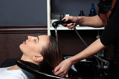 Professional hairdresser washing woman's hair at sink in salon