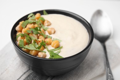 Photo of Tasty chickpea soup in bowl, spoon and napkin on white table, closeup