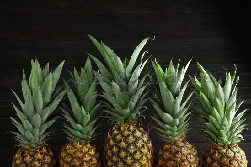 Photo of Fresh ripe juicy pineapples on dark wooden background