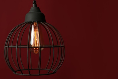 Photo of Hanging lamp bulb in chandelier against dark red background, space for text
