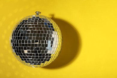 Shiny disco ball on yellow background, top view. Space for text