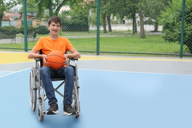 Disabled teenage boy in wheelchair with basketball ball at outdoor court