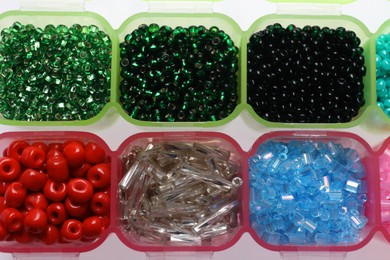 Plastic organizers with different beads on white background, top view