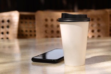 Takeaway coffee cup and smartphone on beige table in cafe