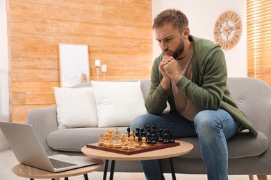 Thoughtful young man playing chess with partner through online video chat in living room