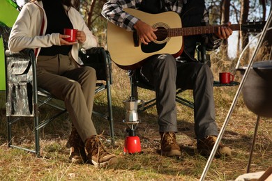 Photo of Couple with guitar resting in camping chairs outdoors, closeup