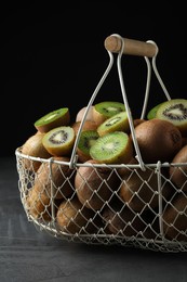 Fresh ripe kiwis in metal basket on grey table against dark background