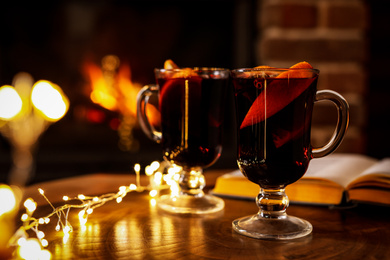 Tasty mulled wine, festive lights and blurred fireplace on background