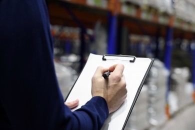 Manager writing in clipboard at warehouse, closeup