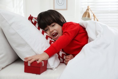 Excited little boy finding gift box under pillow in bed at home. Saint Nicholas day tradition