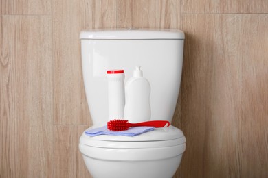 Photo of Bottles, brush and rag on toilet bowl indoors. Cleaning supplies