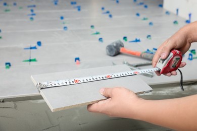 Worker measuring tile near adhesive mix on floor, closeup