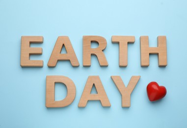 Phrase Earth Day made with wooden letters and red heart on light blue background, flat lay