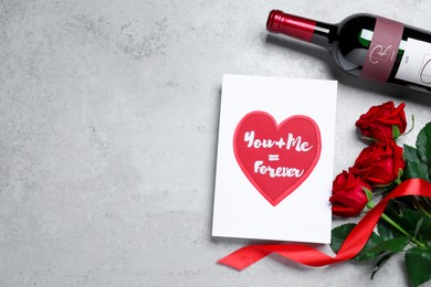 Marvelous message of love with red roses and wine on grey table, flat lay. Space for text