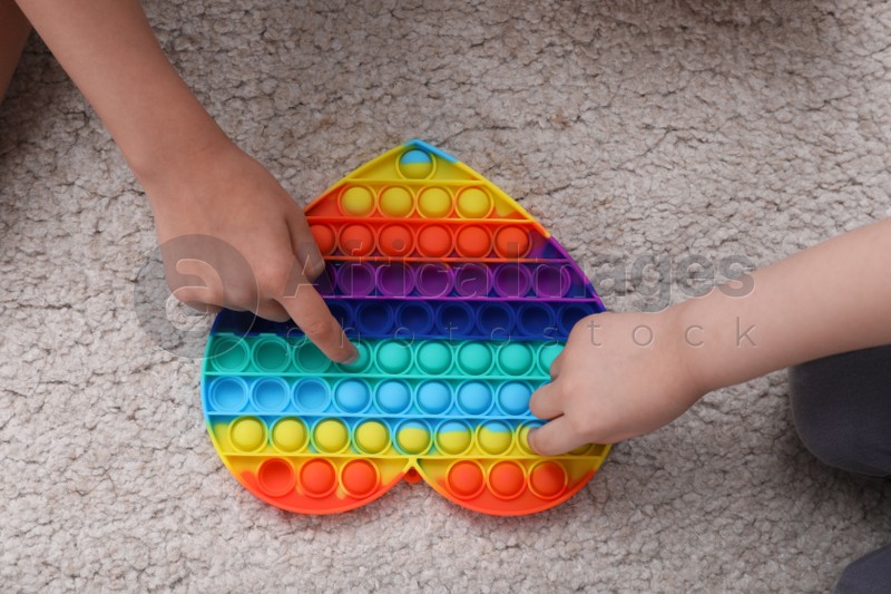Little children playing with pop it fidget toy on floor, top view