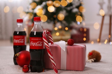 MYKOLAIV, UKRAINE - JANUARY 13, 2021: Bottles of Coca-Cola, candy cane, gift box and Christmas balls on floor in room