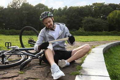 Man applying bandage onto his knee near bicycle outdoors