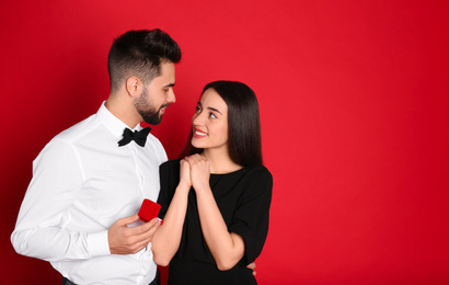 Man with engagement ring making marriage proposal to girlfriend on red background