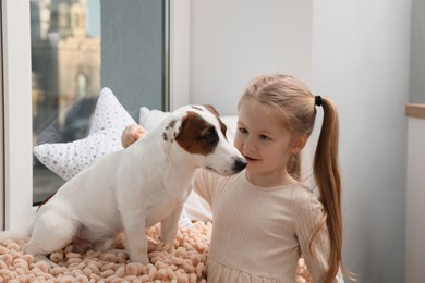Cute little girl with her dog near window at home. Childhood pet