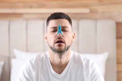 Photo of Man with clothespin suffering from runny nose in bedroom
