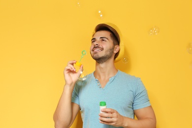 Photo of Young man blowing soap bubbles on color background. Space for text