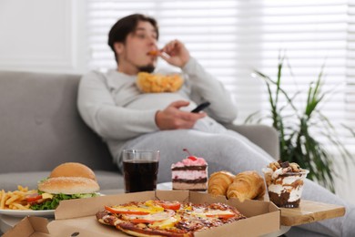Overweight man with chips watching TV at home, focus on junk food