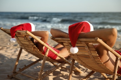 Lovely couple with Santa hats relaxing on deck chairs at beach. Christmas vacation