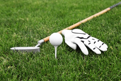 Golf club with ball, tee and glove on green grass
