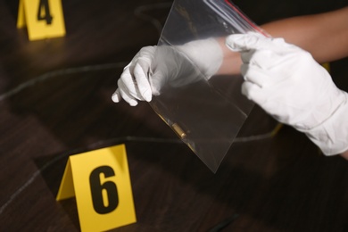 Detective holding plastic bag with bullet shell at crime scene, closeup